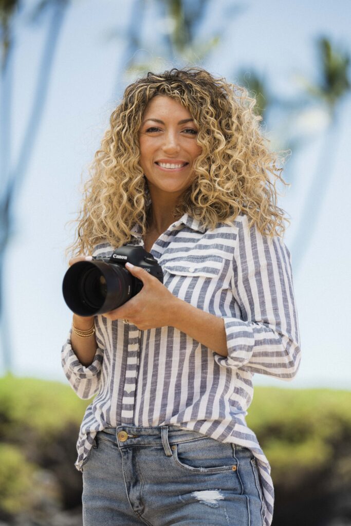 Warm, professional portrait of Jaclyn holding her camera on a sunny Hawaiian beach, radiating confidence as a Ventura County-based personal brand photographer.