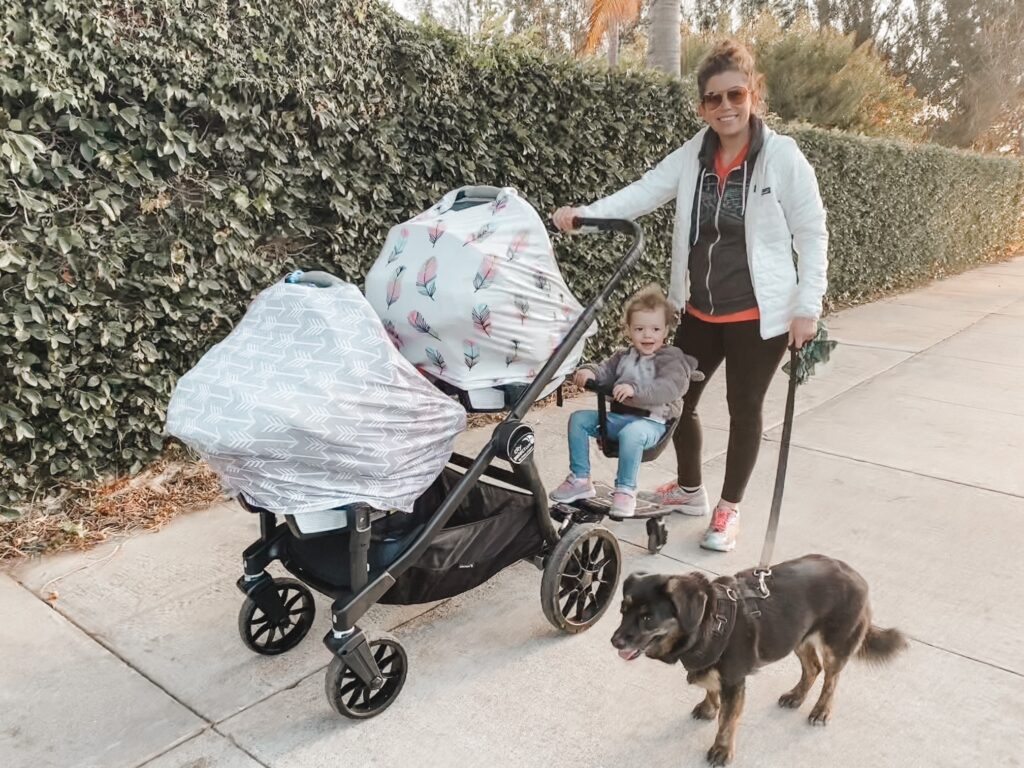 Jaclyn smiling on a neighborhood walk with her toddler daughter, twins covered in their stroller, and family dog, capturing her real-life balance of motherhood and business.