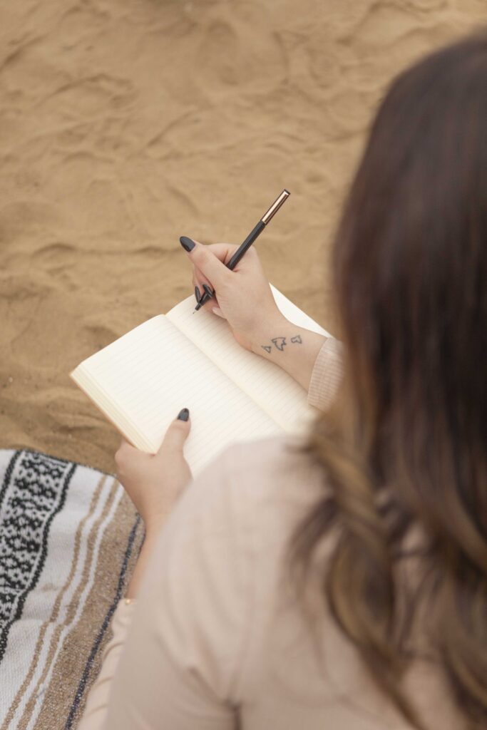 Close-up of a woman journaling during a beachside brand session, showcasing intentional self-reflection.