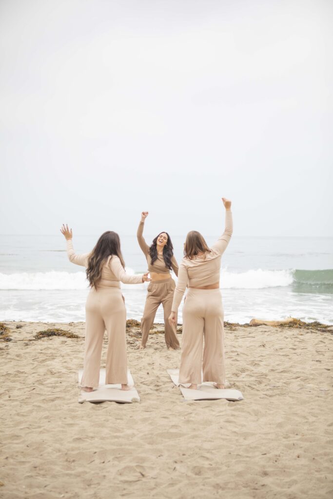 Kristine King dancing joyfully with two women on the beach, celebrating freedom and embodiment.