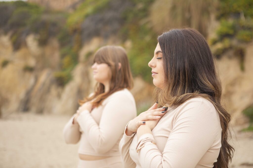 Two women with hands on hearts, standing in peaceful meditation during Kristine King’s brand session.