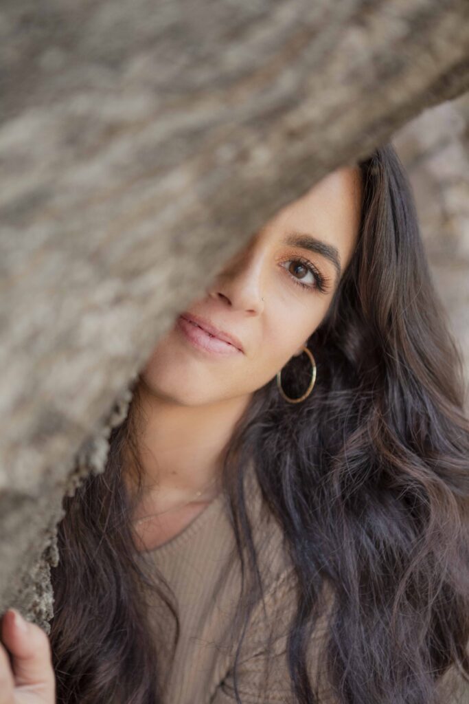 Close-up portrait of Kristine King peeking through a tree trunk, symbolizing self-reflection and growth.