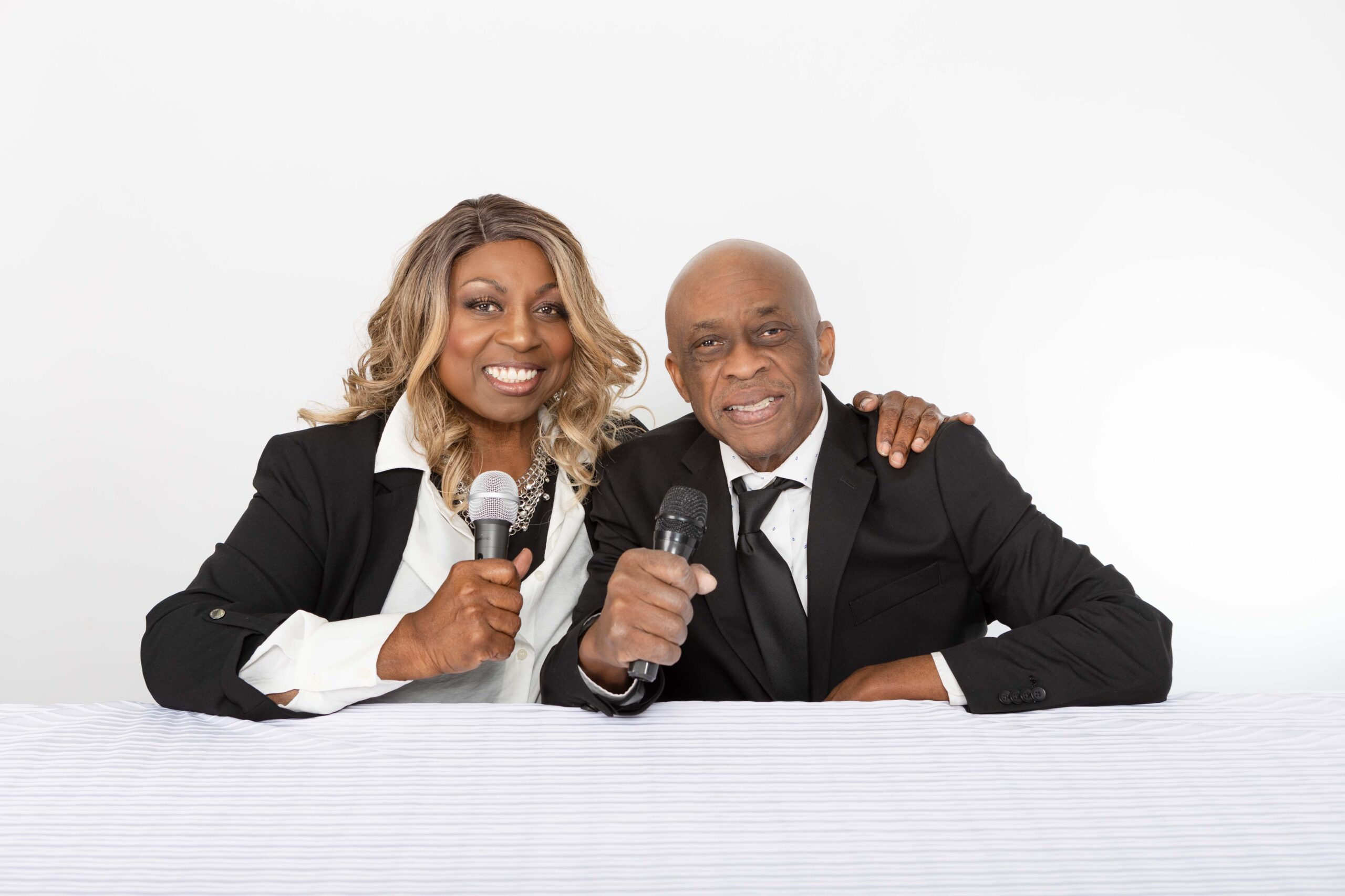 Denise Carter and her husband Wills seated at a table holding microphones during a studio podcast branding photoshoot.