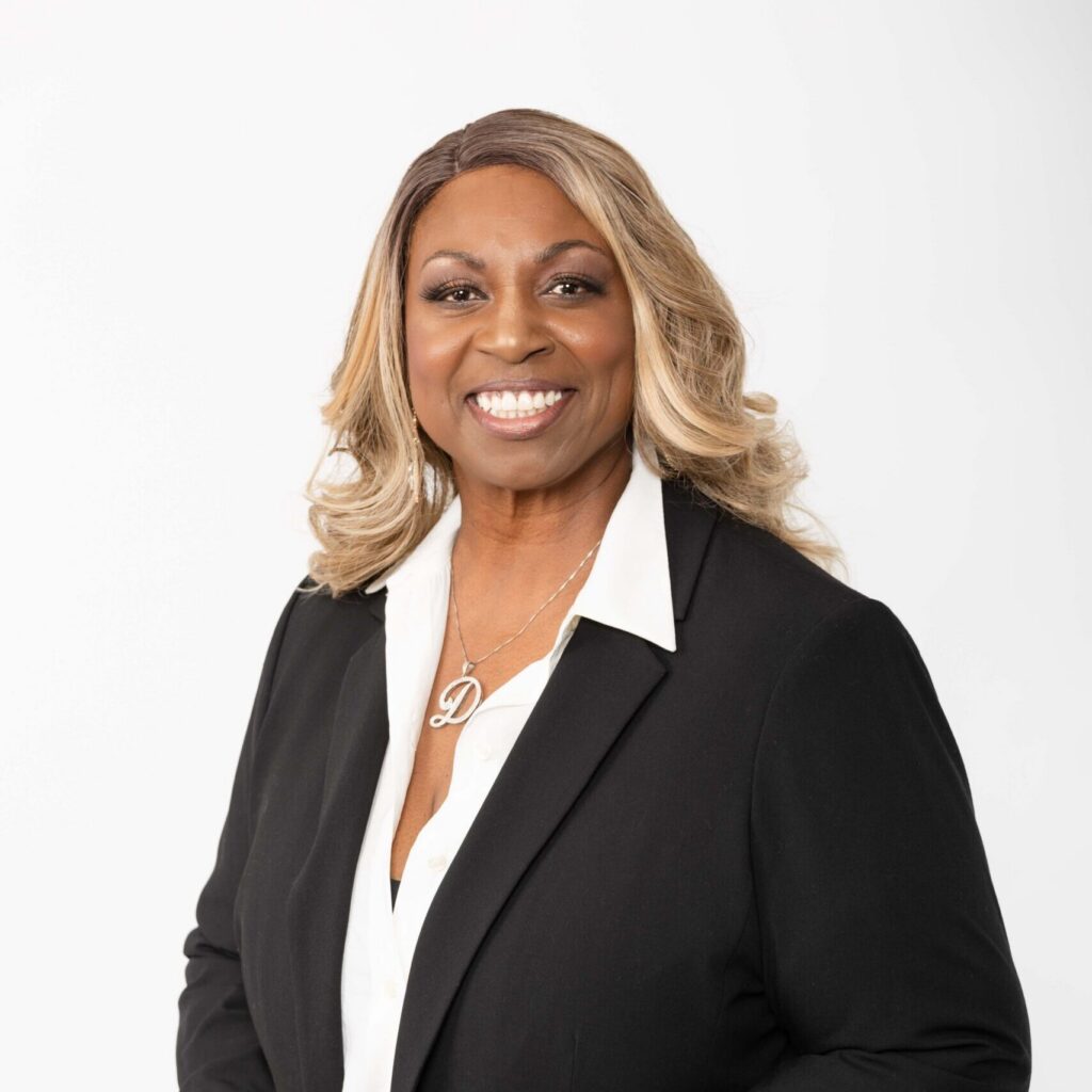 Professional studio headshot of Denise Carter smiling in a black blazer and white blouse against a white background.